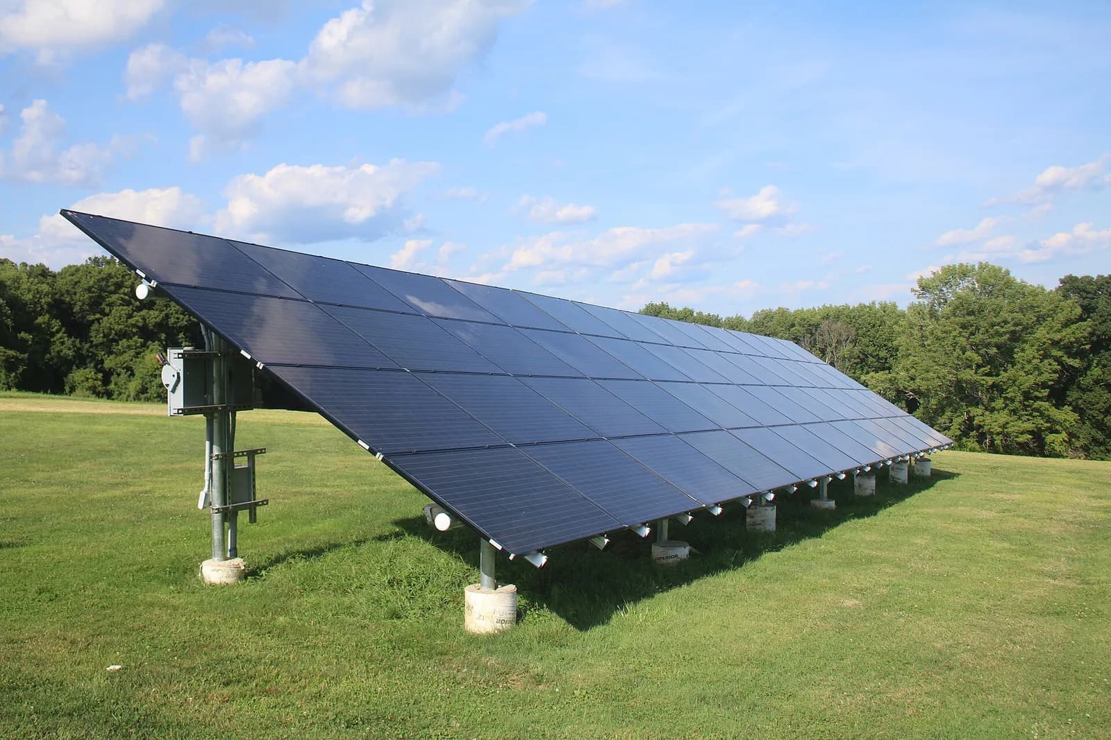 Photograph of a ground-mounted solar panel array under a blue sky